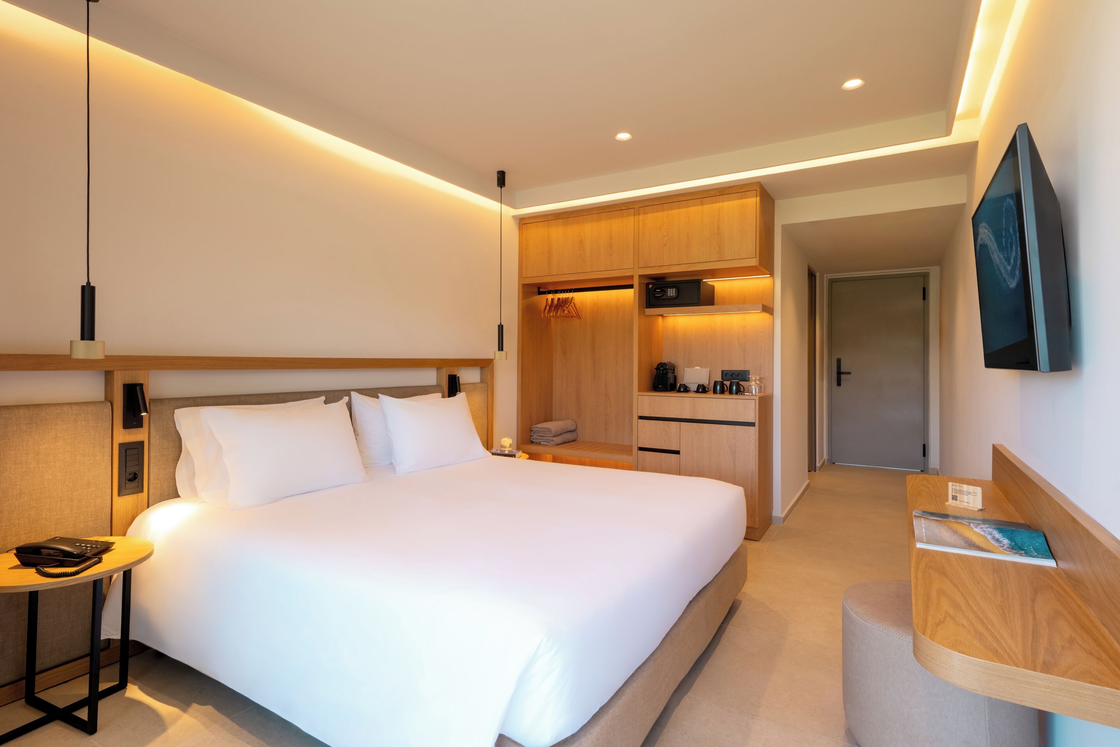 Ein modernes Hotelzimmer mit einem großen Bett, einem Schreibtisch, einer Küchenzeile und einem an der Wand montierten Fernseher.