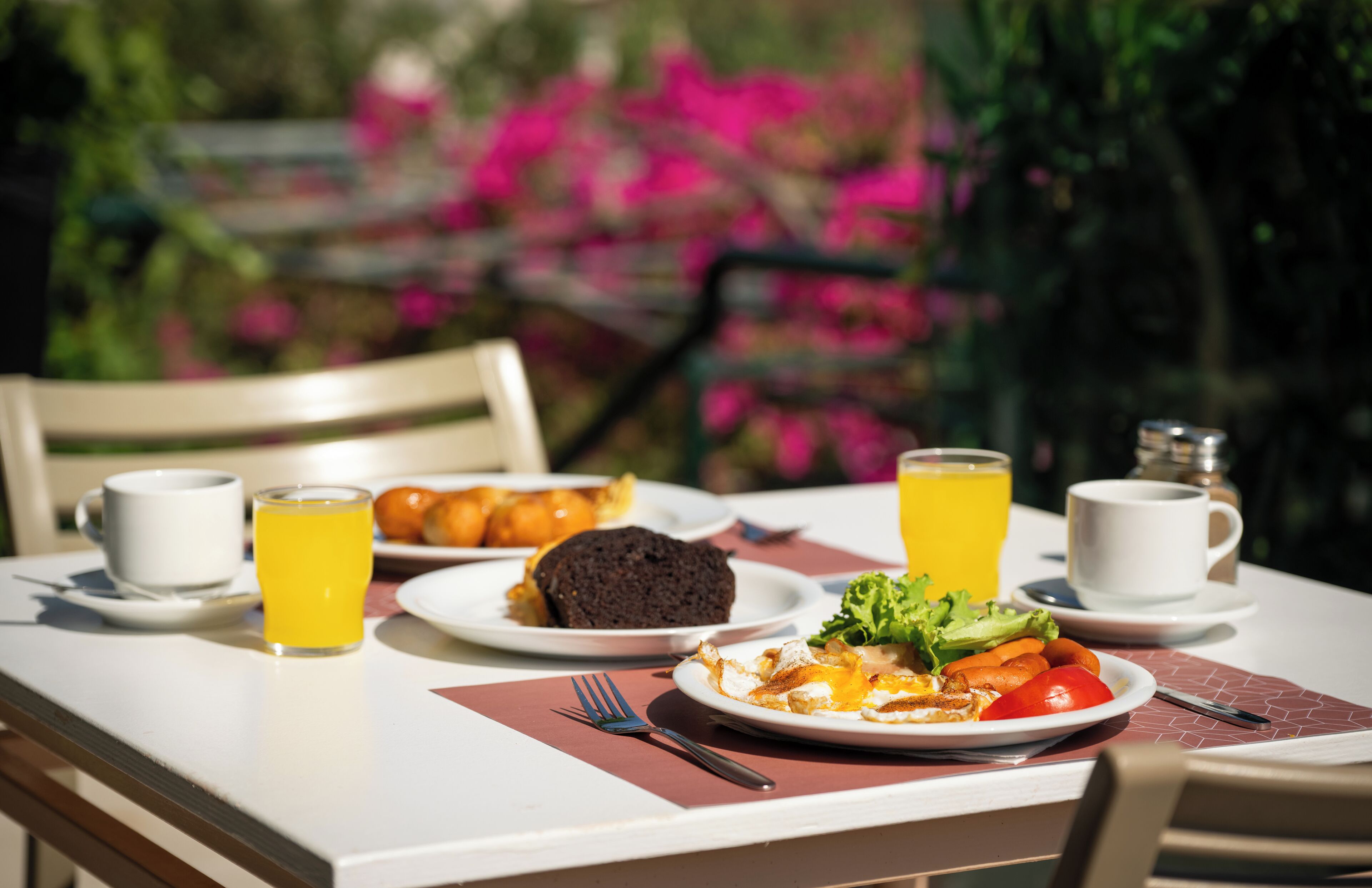 A table with breakfast items including toast, eggs, and orange juice, set outdoors with a chair and a table mat.