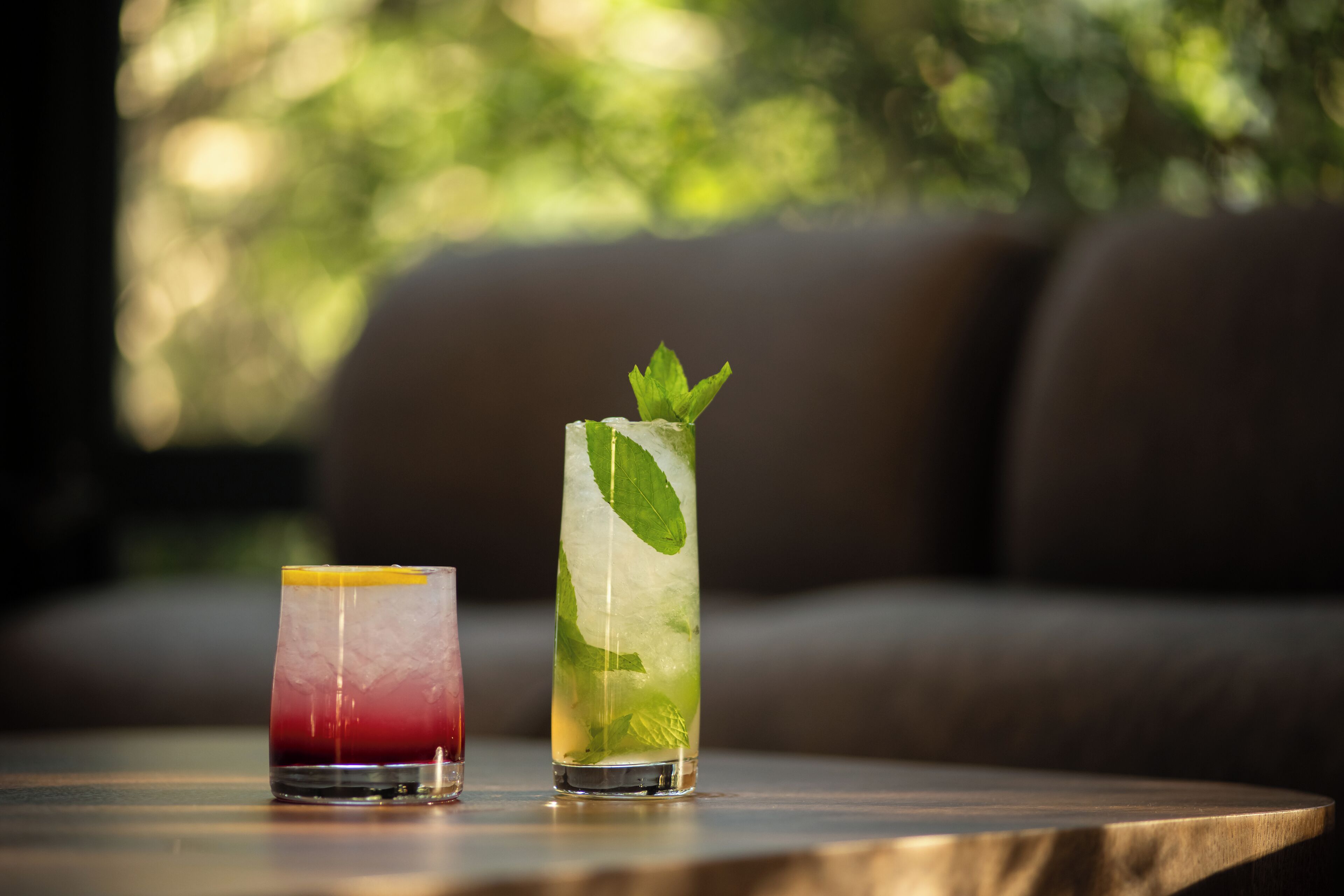 Two drinks on a table with a blurred outdoor background.