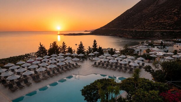 Un complexe hôtelier doté d’une piscine, de chaises longues, de parasols et offrant une vue sur le coucher de soleil en mer.
