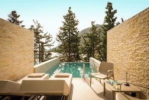 A poolside area with lounge chairs and a table, surrounded by stone walls and trees.