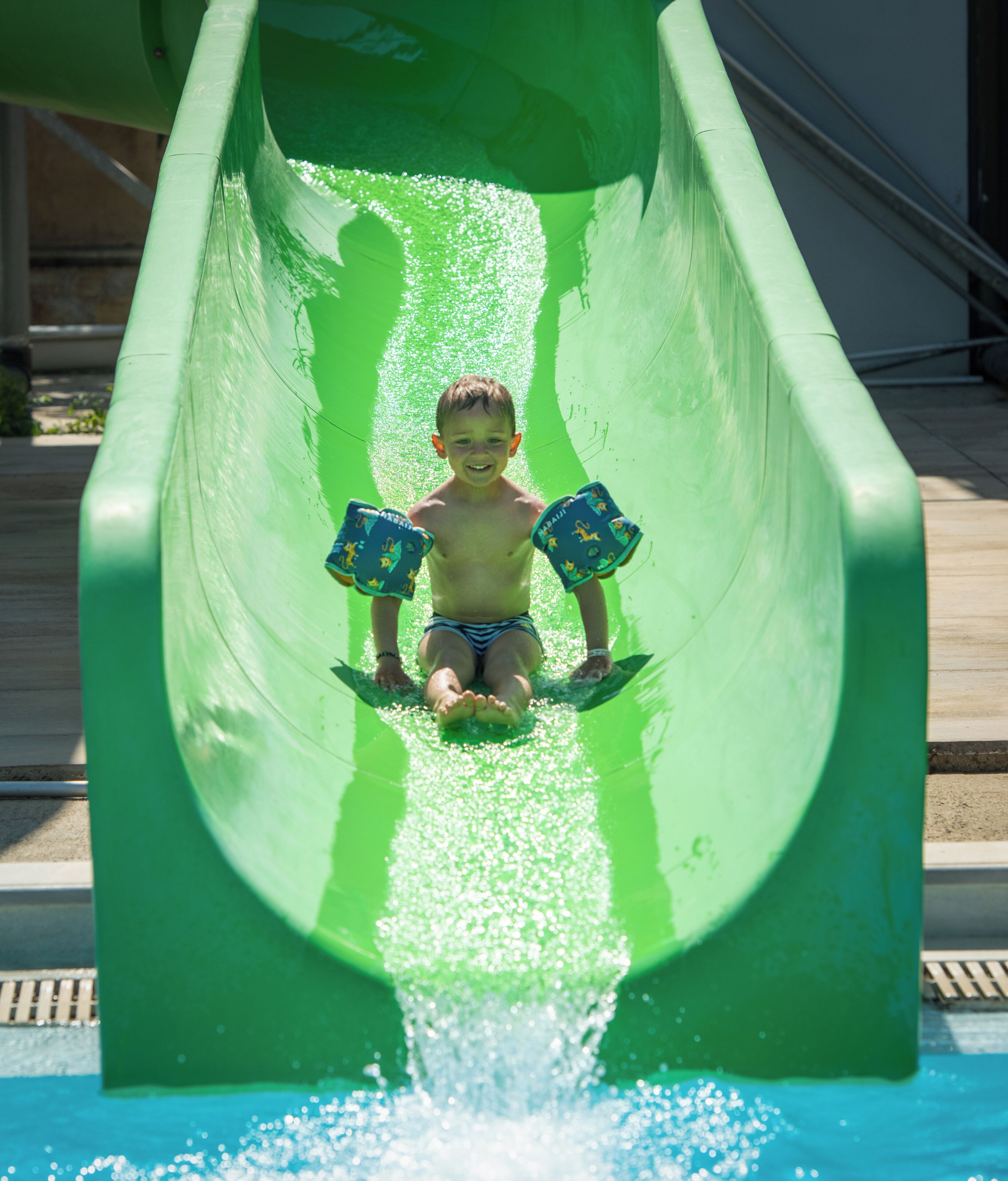 Un niño deslizándose por un tobogán de agua verde.