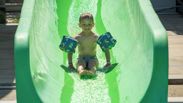 Un niño deslizándose por un tobogán de agua verde.