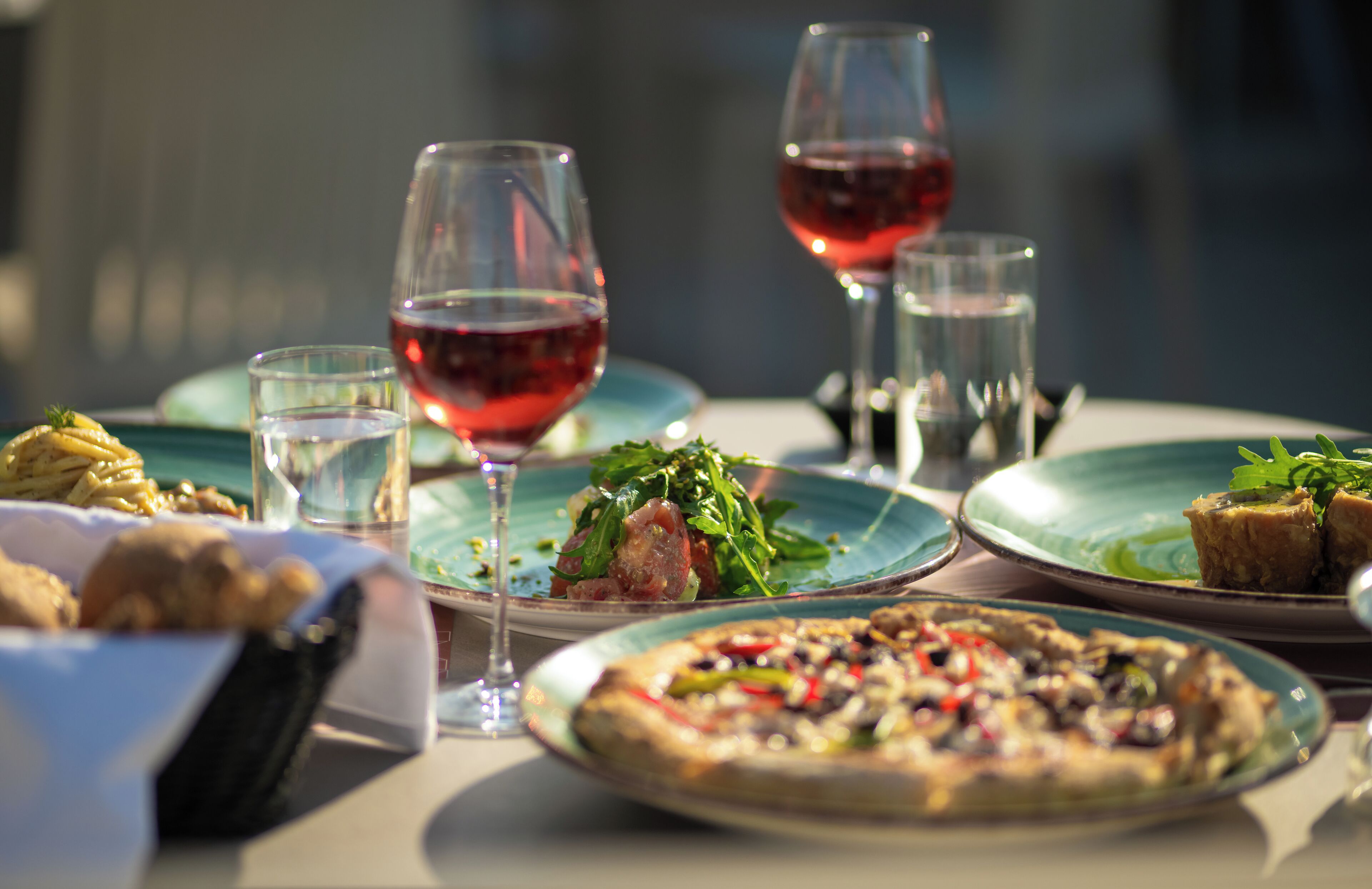 A table set with various dishes, including pizza and salads, and two glasses of red wine.