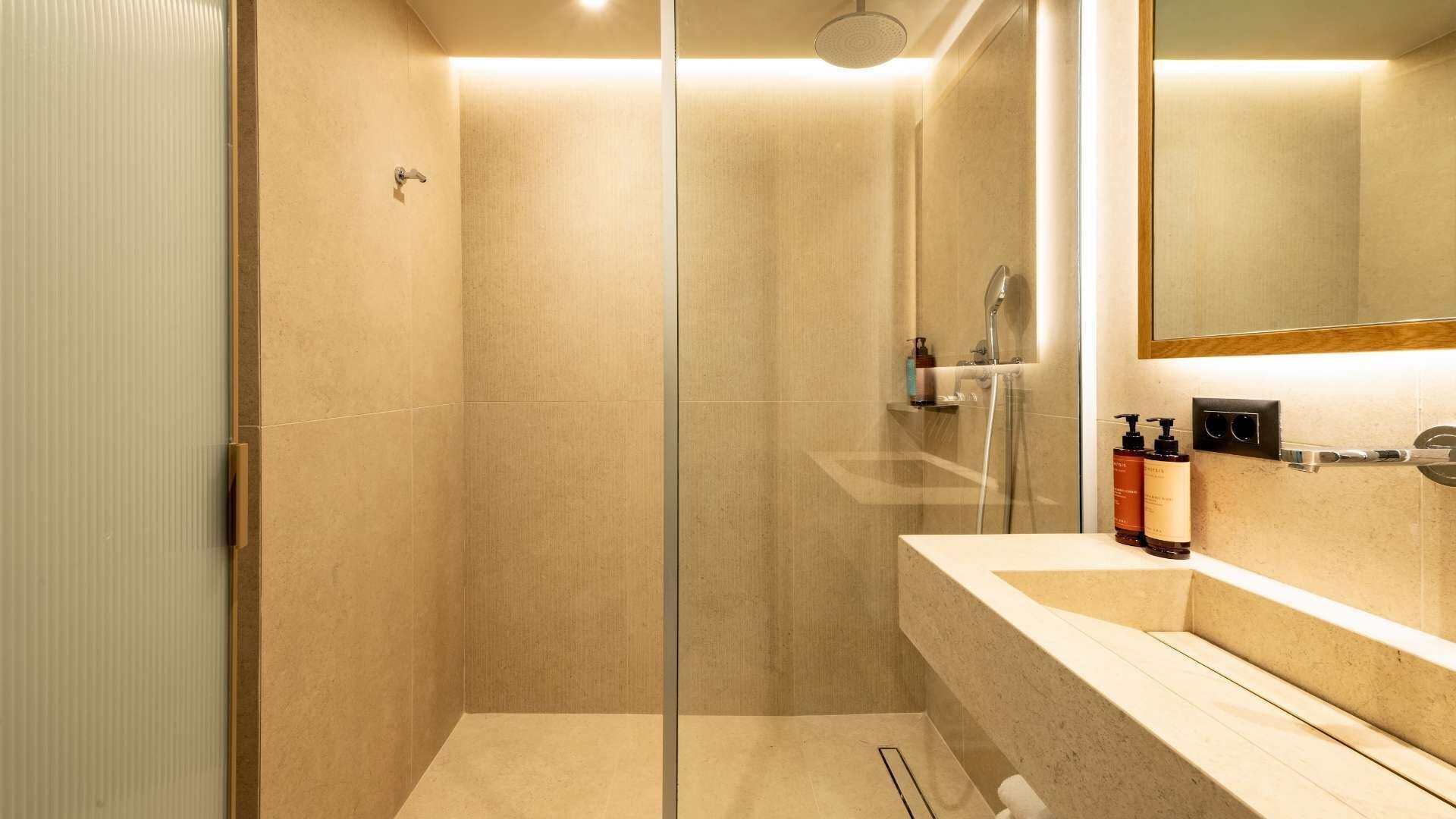 A modern bathroom with a glass shower enclosure, a vanity with a mirror, and toiletries.