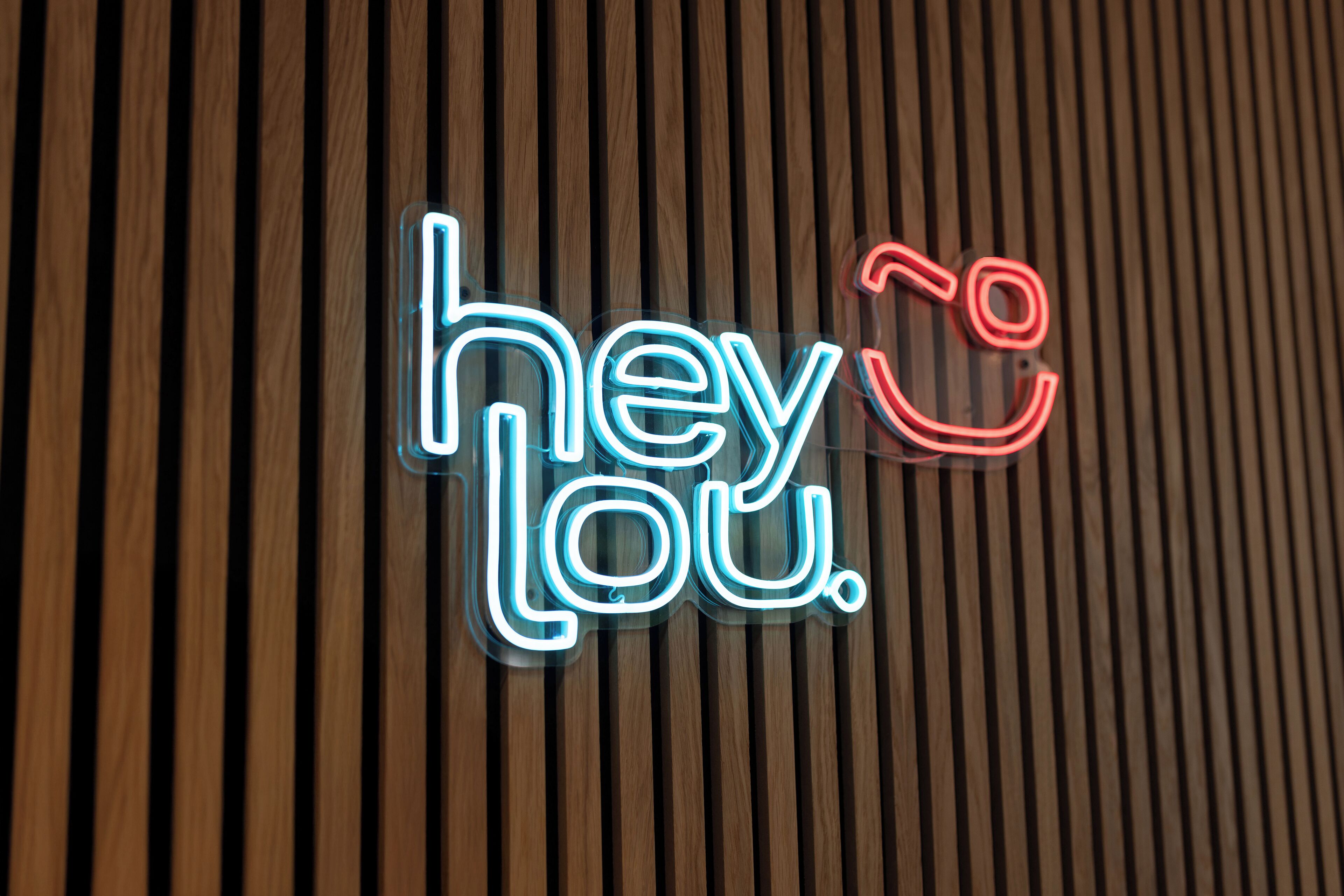 Un letrero de neón con el texto 'hey Lou' sobre un fondo de madera.