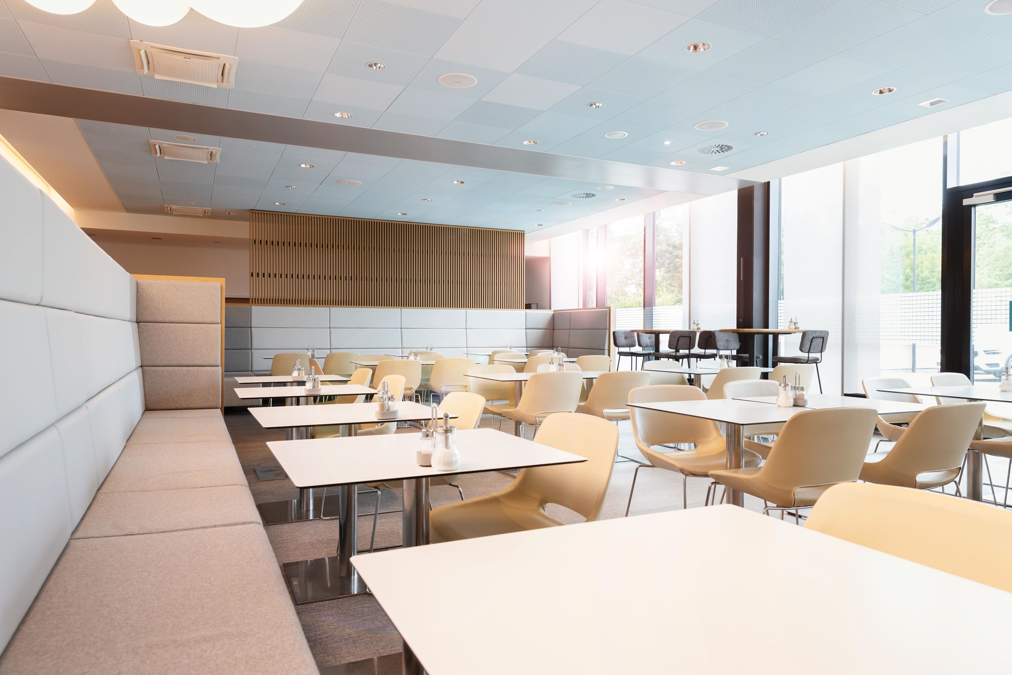 A modern dining area with tables and chairs, a long bench, and a large window providing natural light.