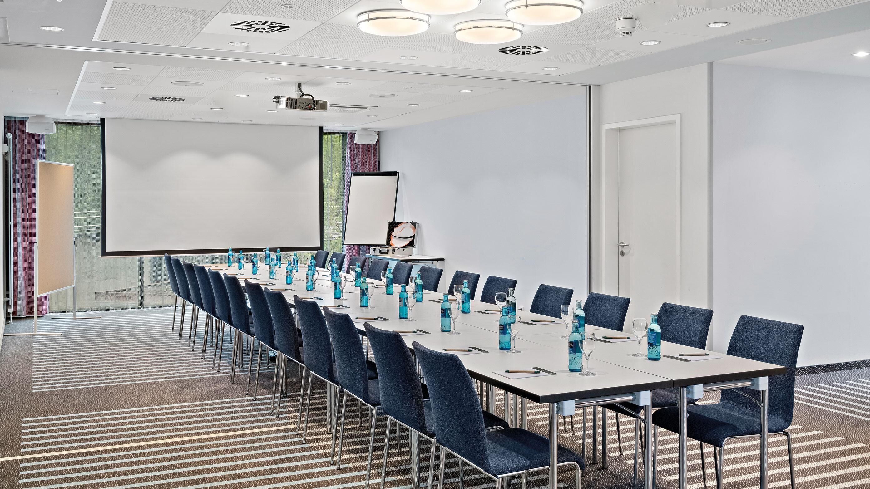 Uma sala de conferências com uma mesa comprida, cadeiras, um projetor e uma tela.