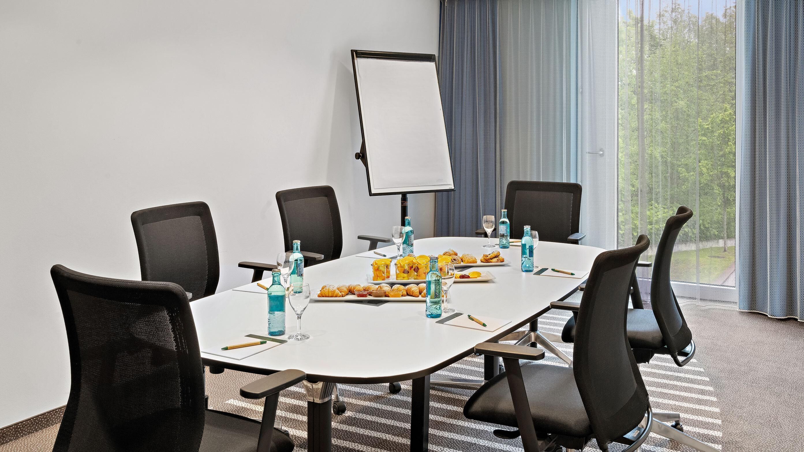 A conference room with a whiteboard, black chairs, a table with water bottles, glasses, and pastries.