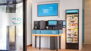 Un espace d’accueil doté d’un écran numérique affichant le message « hey lou » et d’un distributeur automatique portant l’inscription « Lou’s SmartBox ».
