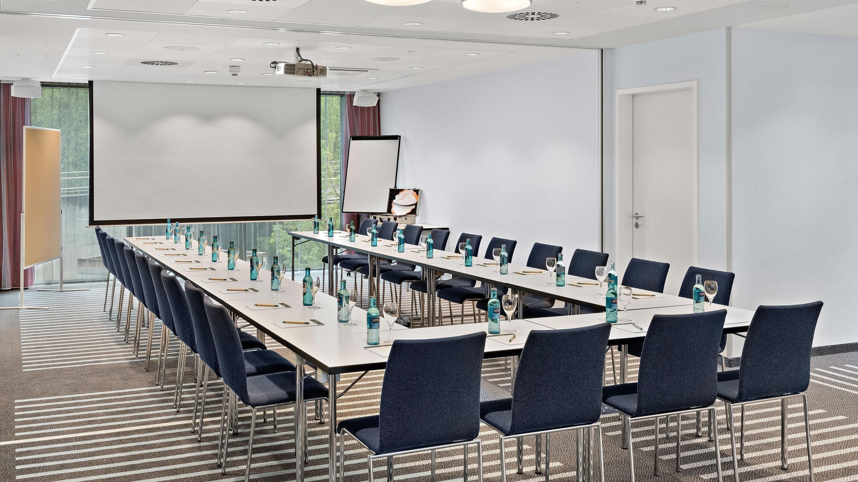 Une salle de conférence équipée d’une longue table, de chaises, d’un projecteur et d’un écran.
