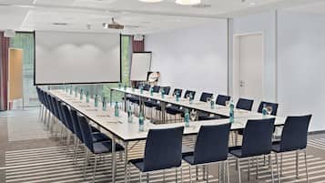Une salle de conférence équipée d’une longue table, de chaises, d’un projecteur et d’un écran.