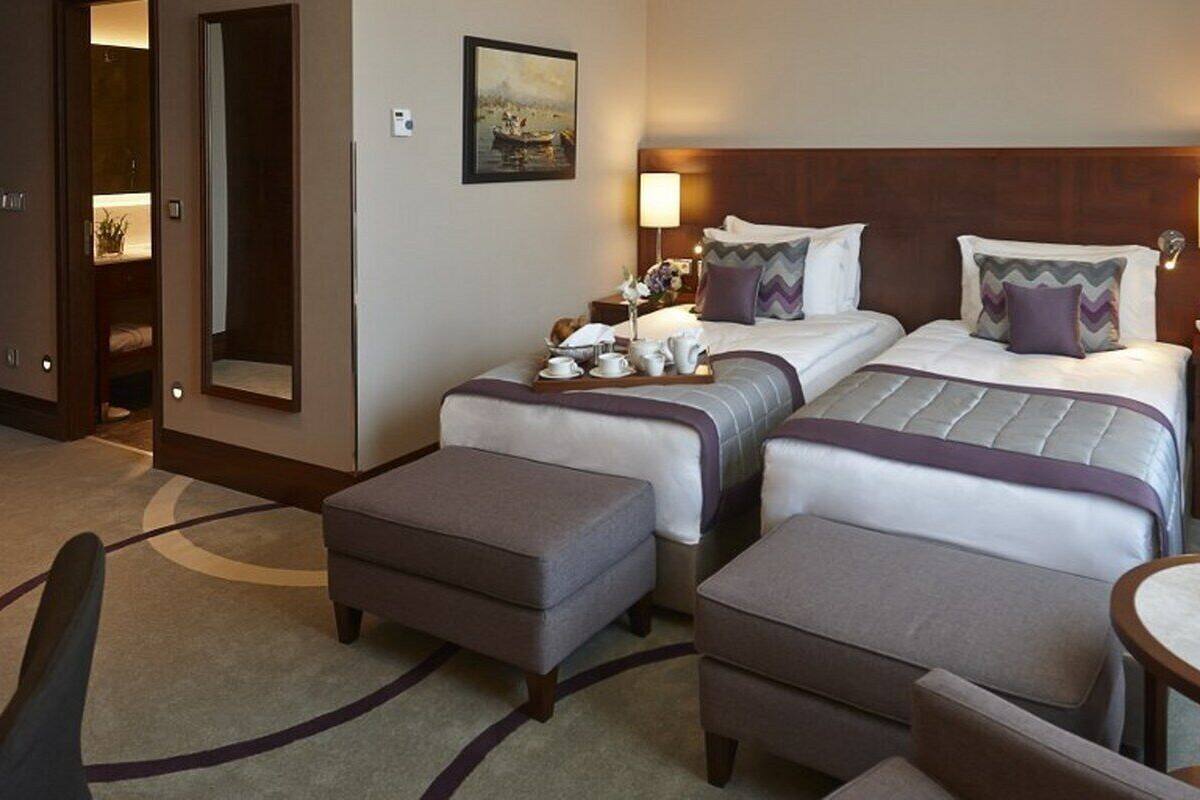 A hotel room with two beds, a sitting area, a small table, and a vase of flowers.