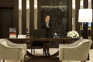 A reception desk with a laptop, a name tag, and a sign for guest relations. There are two chairs in front of the desk and a vase with flowers on the right. - Crowne Plaza Istanbul - Oryapark by IHG (Istanbul)
