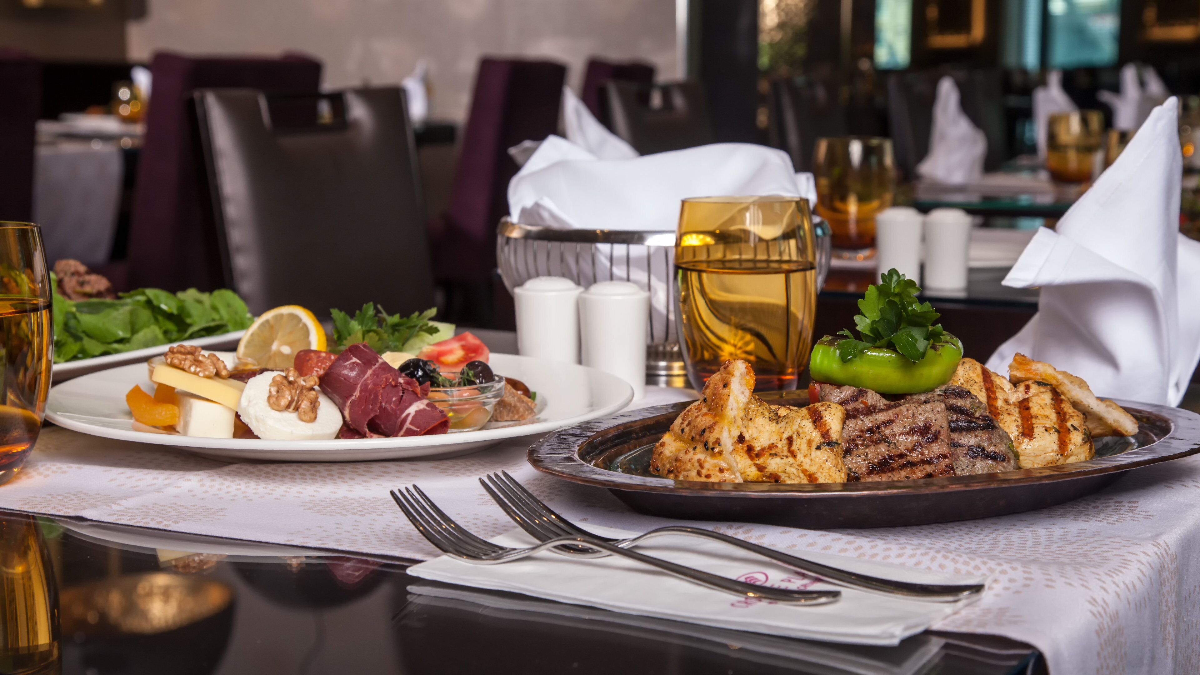 A dining table with plates of food, a glass of beverage, and cutlery.