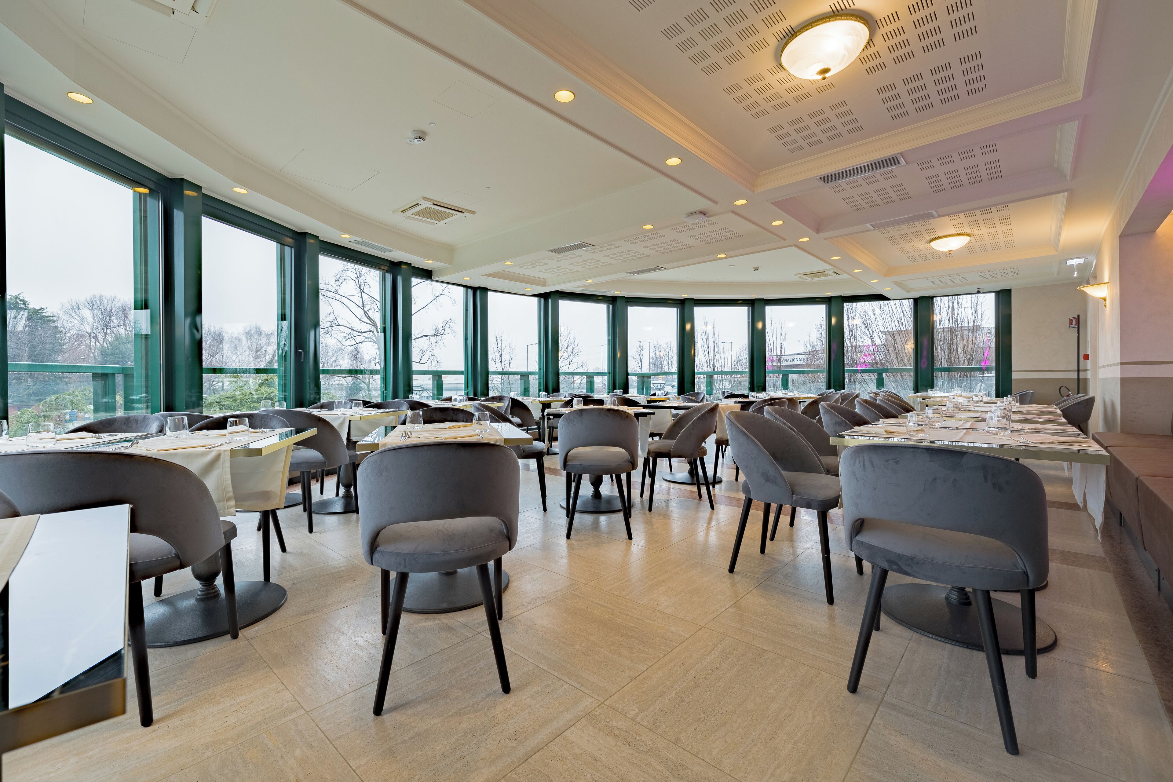 A spacious dining area with large windows, modern chairs, and tables set for dining.