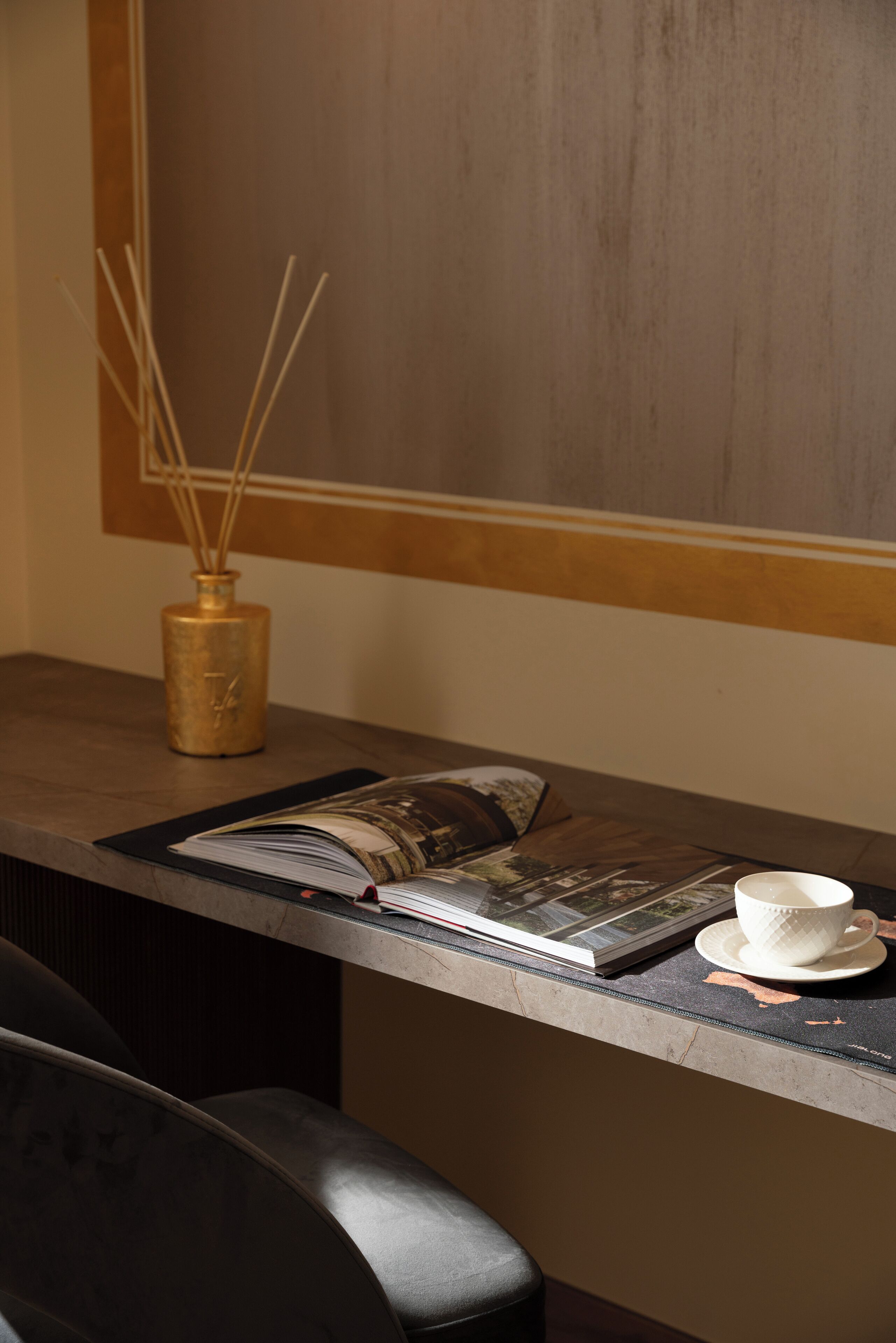 Un escritorio de madera con una revista, una taza blanca y un jarrón decorativo con ramas de junco.