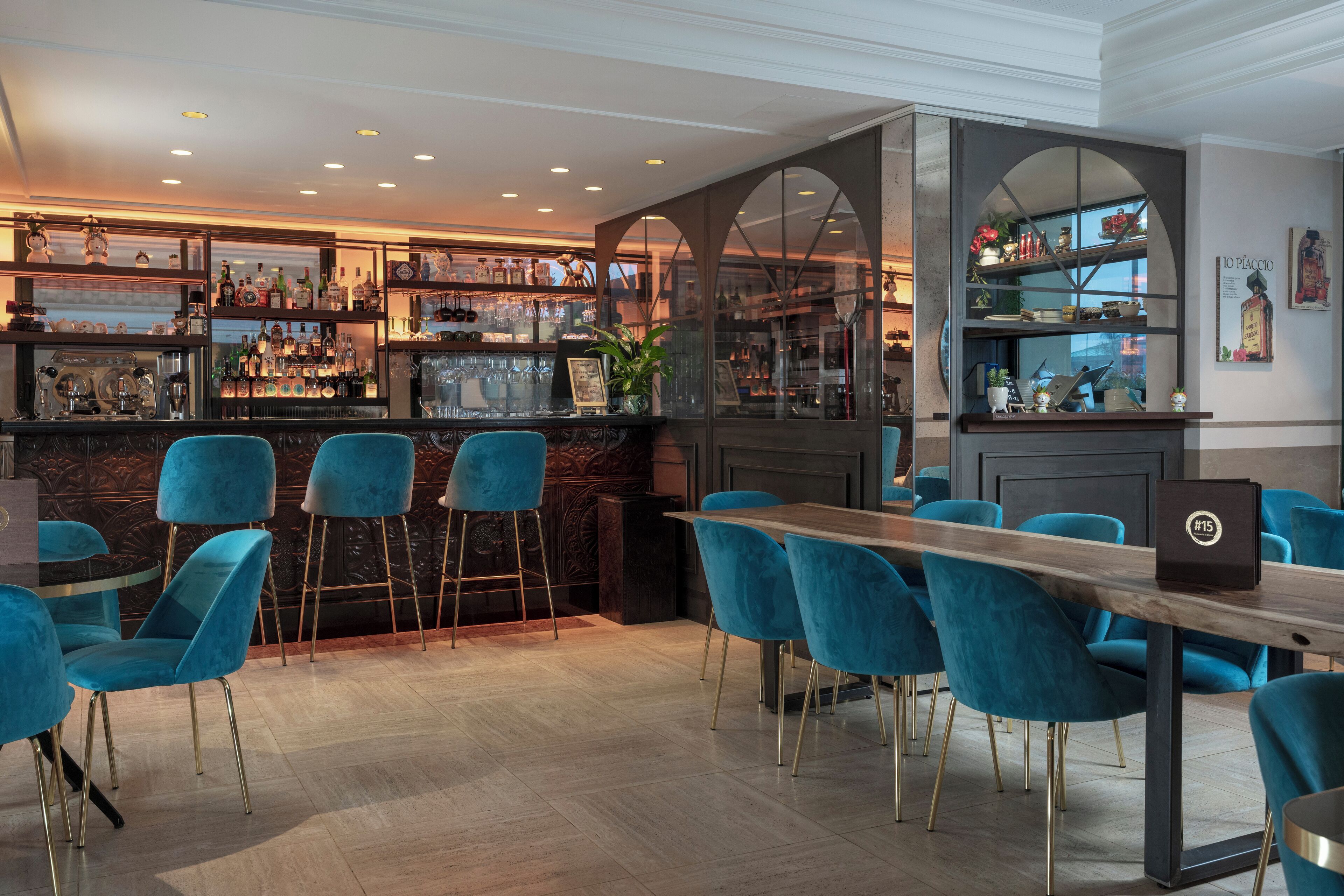A bar area with blue chairs, a wooden table, and shelves stocked with bottles and glasses.