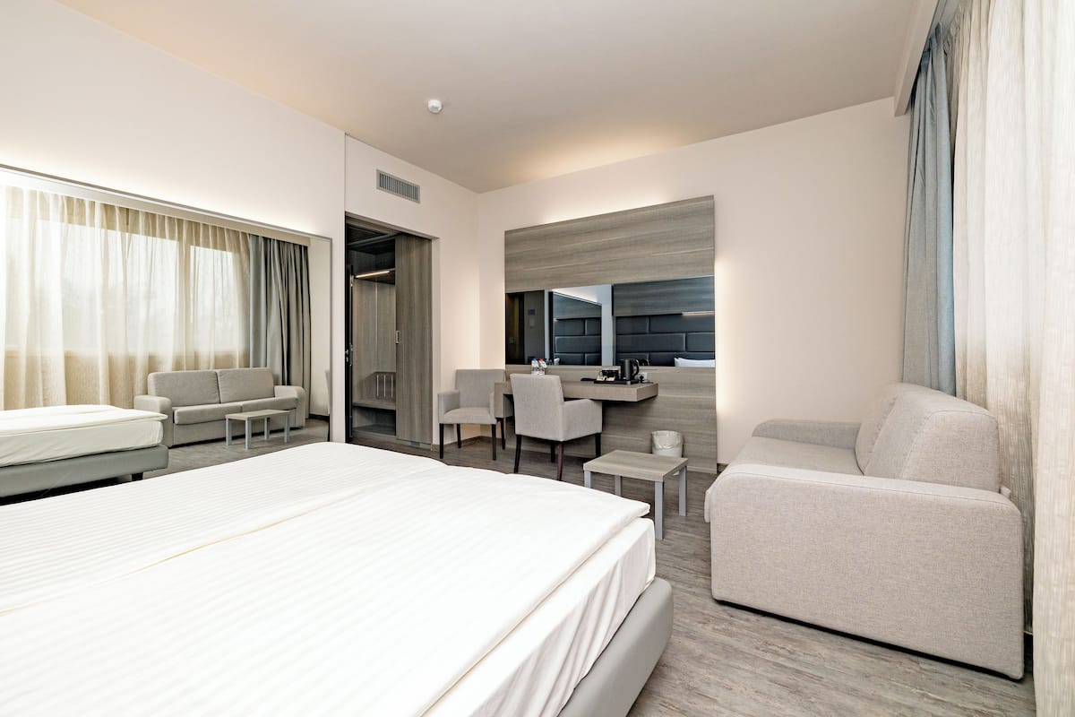A modern hotel room with a large bed, a sofa, a desk, and a chair.