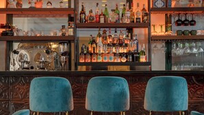 A bar area with blue velvet chairs, a polished bar counter, and shelves stocked with liquor bottles. - Just Hotel Saronno (Saronno)