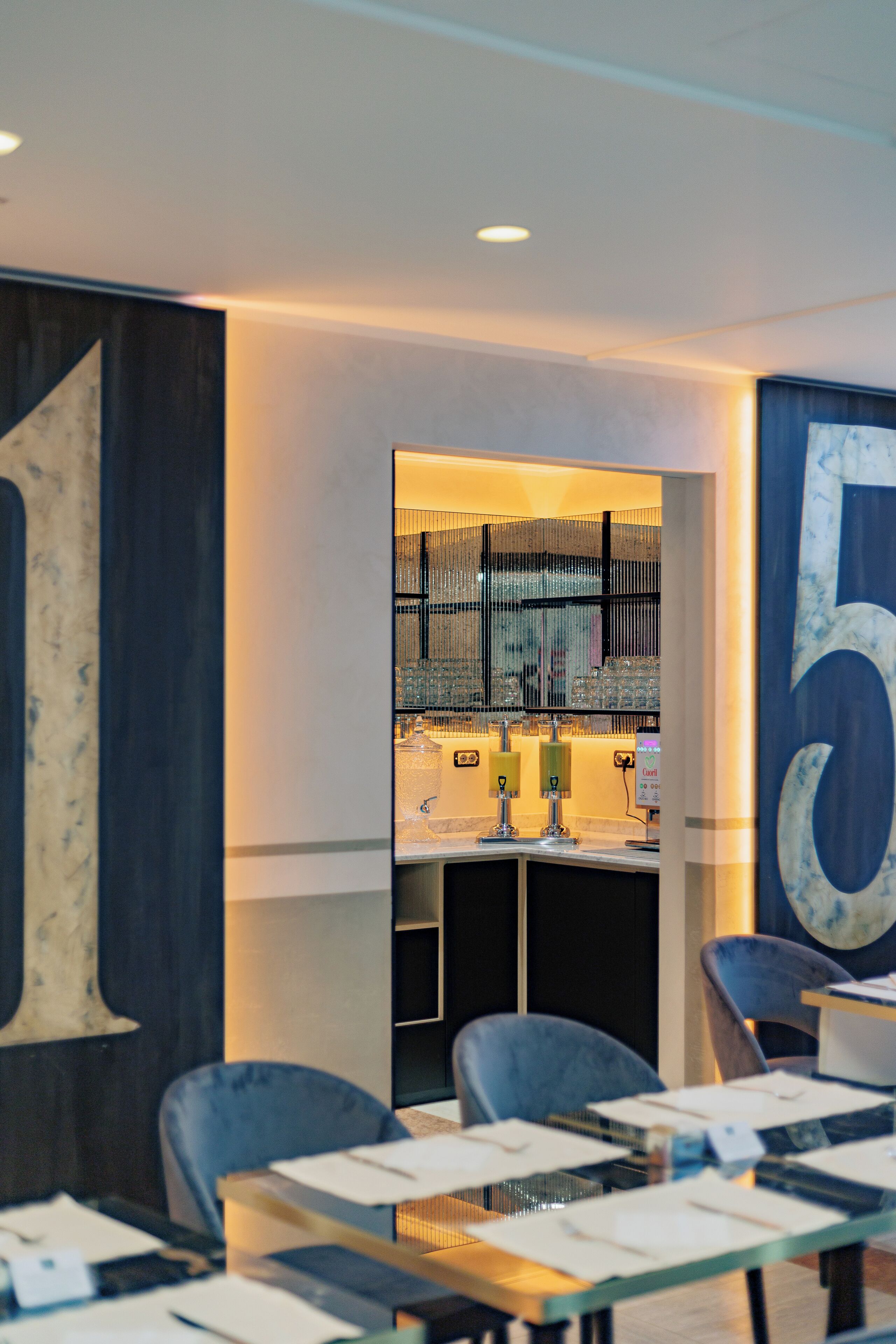 A modern conference room with a glass table, chairs, and a visible kitchen area with a sink and counter.