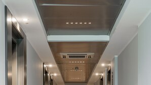 A modern hotel corridor with a carpeted floor, recessed lighting, and fire extinguishers along the walls. - Just Hotel Saronno (Saronno)