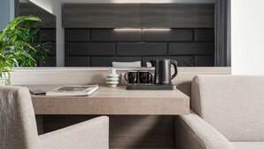 A modern hotel room with a minimalist design, featuring a neutral color palette, a sleek black headboard, and a clean, uncluttered workspace with a coffee maker and a laptop. - Just Hotel Saronno (Saronno)