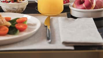 Una mesa de desayuno con un vaso de jugo de naranja, un plato de tomates en rodajas, un tazón de cereal y un plato de pasteles.