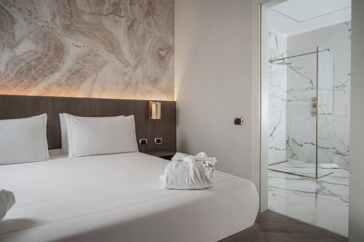 A hotel room with a large bed, a marble wall, and a glass-enclosed shower area.