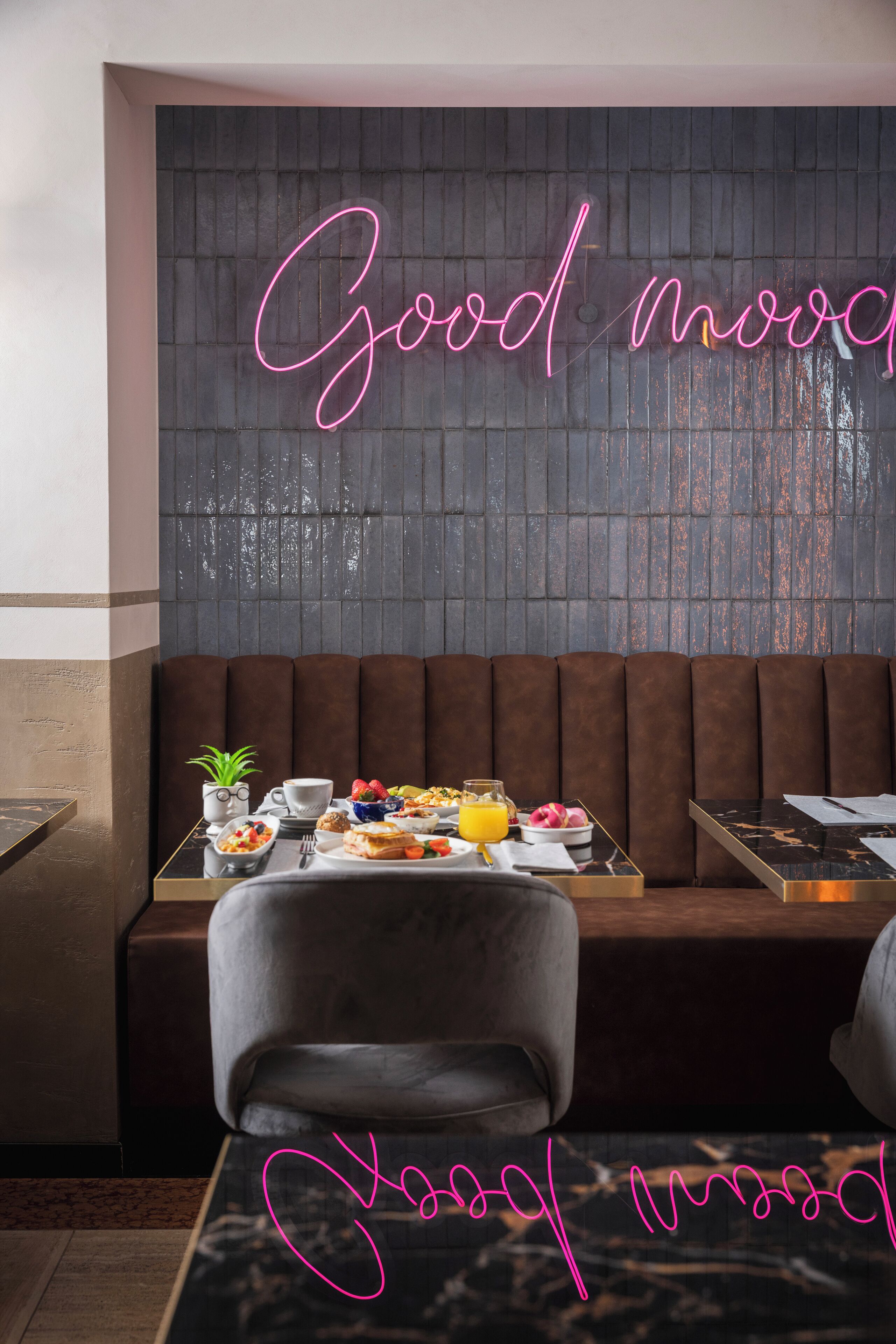 A restaurant interior with a neon sign reading "Good morning," a brown cushioned bench, and a table set with various dishes and drinks.