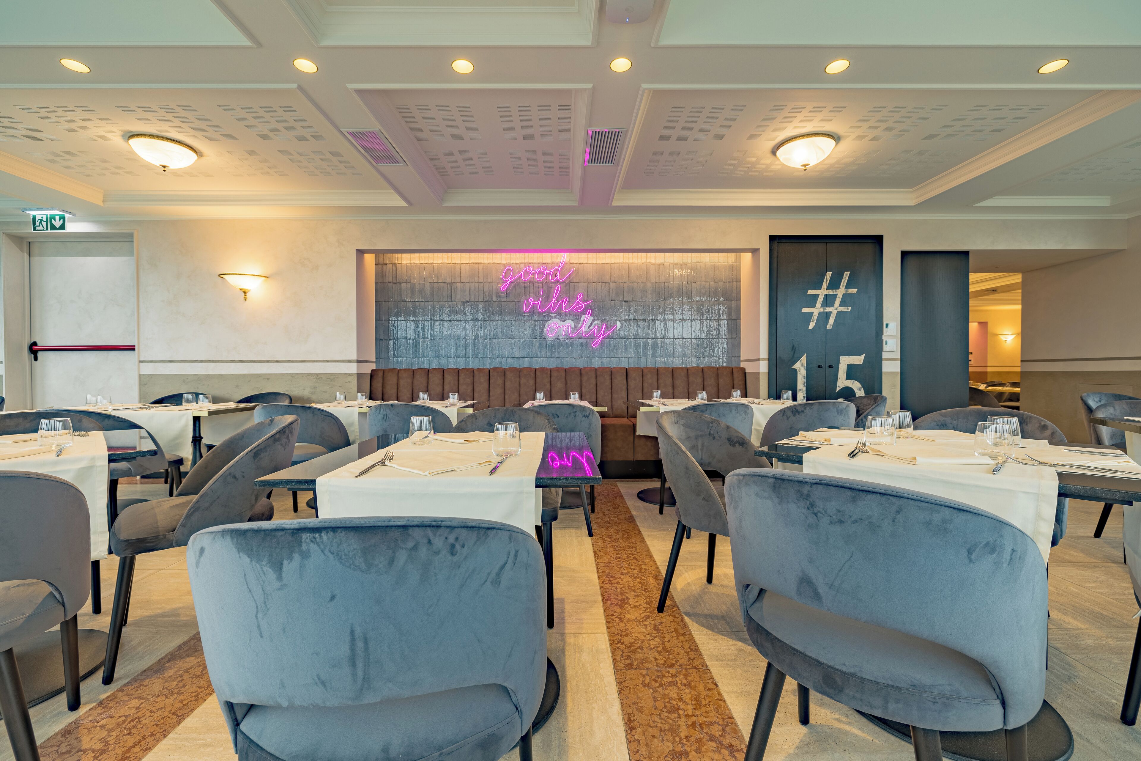 Un restaurante con mesas dispuestas para comer, un letrero de neón que dice 'good vibes only' y una puerta marcada con un símbolo de hashtag.