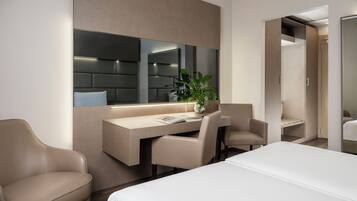 Een moderne hotelkamer met een bed, een bureau, twee stoelen, een grote spiegel en een potplant.