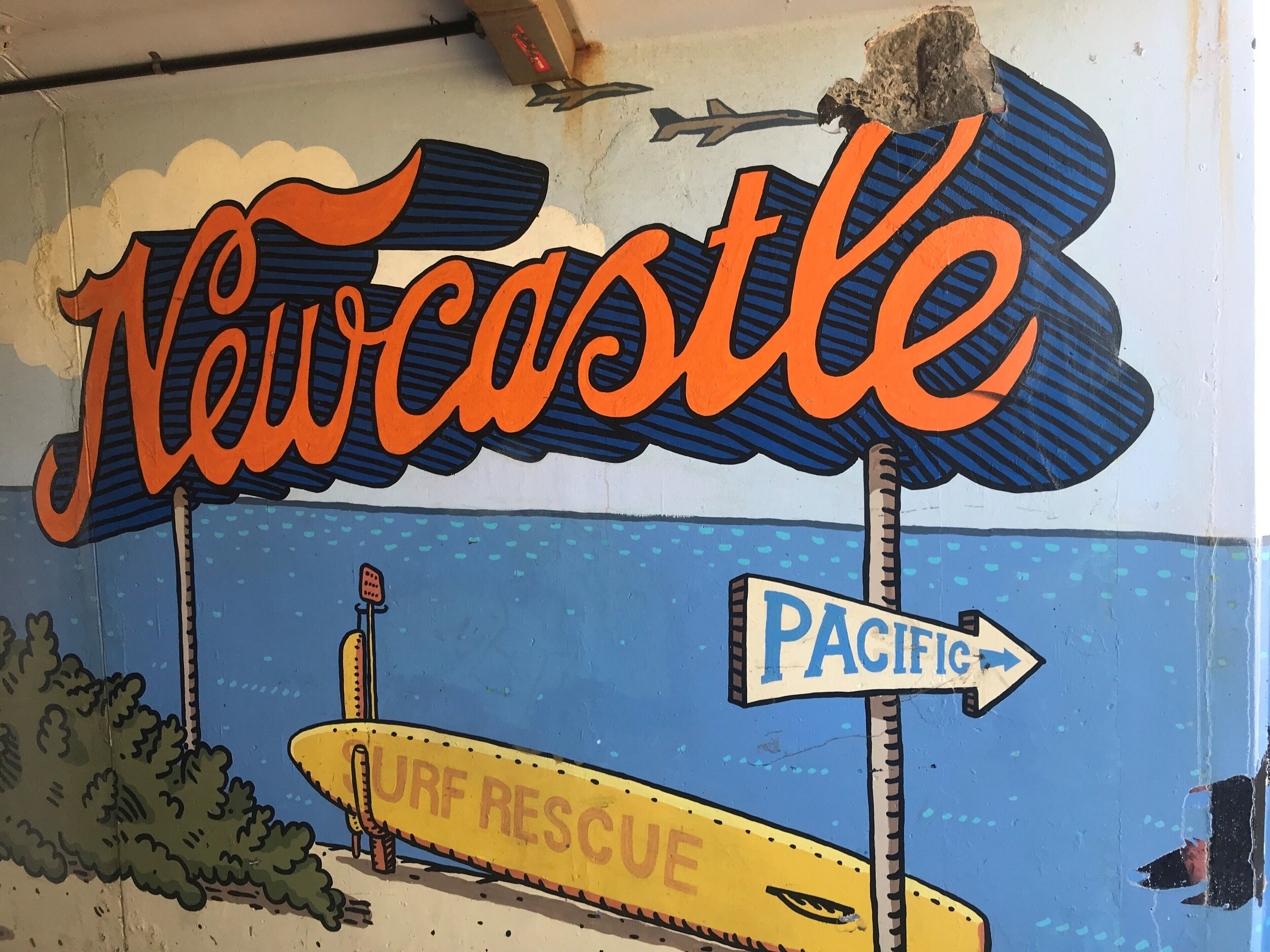 Un mural con la palabra 'Newcastle' y una embarcación de rescate para surfistas.