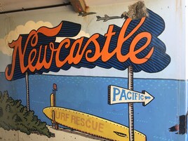 Un mural con la palabra 'Newcastle' y una embarcación de rescate para surfistas.