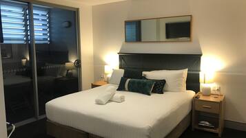 Una habitación de hotel con una cama grande, dos mesitas de noche con lámparas, un espejo sobre la cama y una puerta corredera que da a otra habitación.