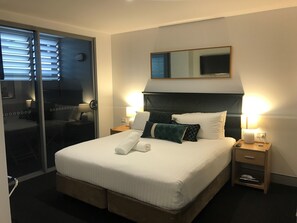 A hotel room with a large bed, two bedside tables with lamps, a mirror above the bed, and a sliding door leading to another room. - Crown on Darby (Cooks Hill)