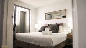 Et hotelværelse med en seng, sengeborde med lamper, et spejl og en dør til en balkon.