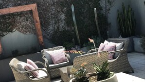 En udendørs terrasse med fletmøbler, et betonbord og en potteplante.