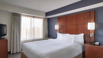 A hotel room with a large bed, a wooden headboard, two bedside lamps, a TV on a wooden cabinet, and a window with curtains.