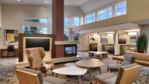 A spacious lounge area with a fireplace, comfortable seating, and large windows offering views of the outdoors. - Residence Inn by Marriott Greenville (Greenville)