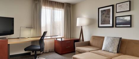A hotel room with a desk, a TV, a sofa, and a window with curtains.