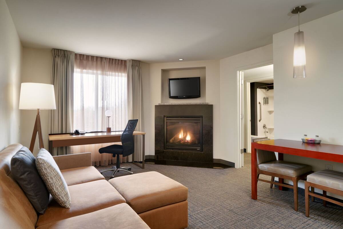 Una habitación de hotel moderna con sofá, escritorio, chimenea y televisor.