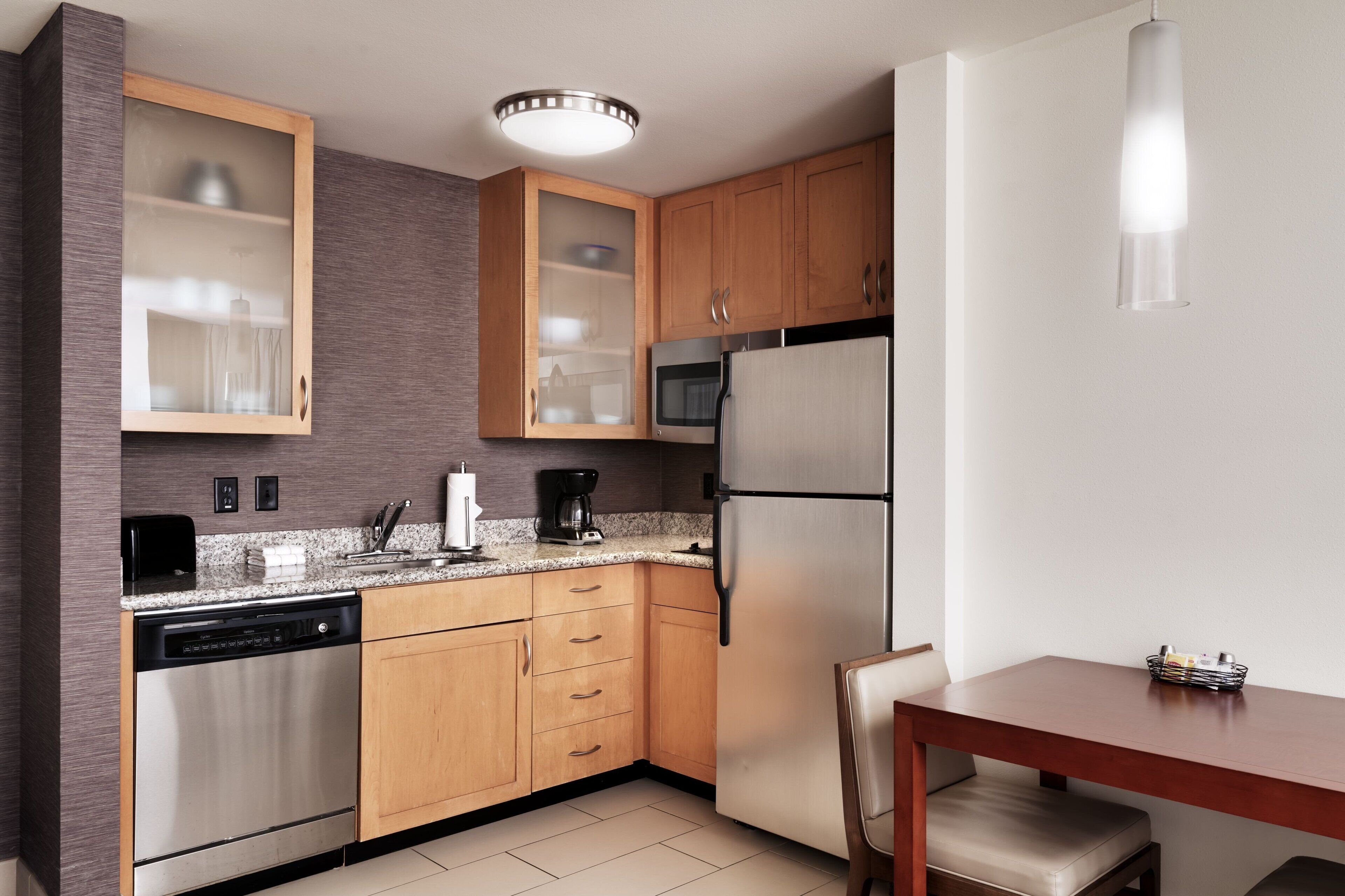 A compact kitchen with wooden cabinets, a built-in microwave, a stainless steel refrigerator, and a dishwasher.