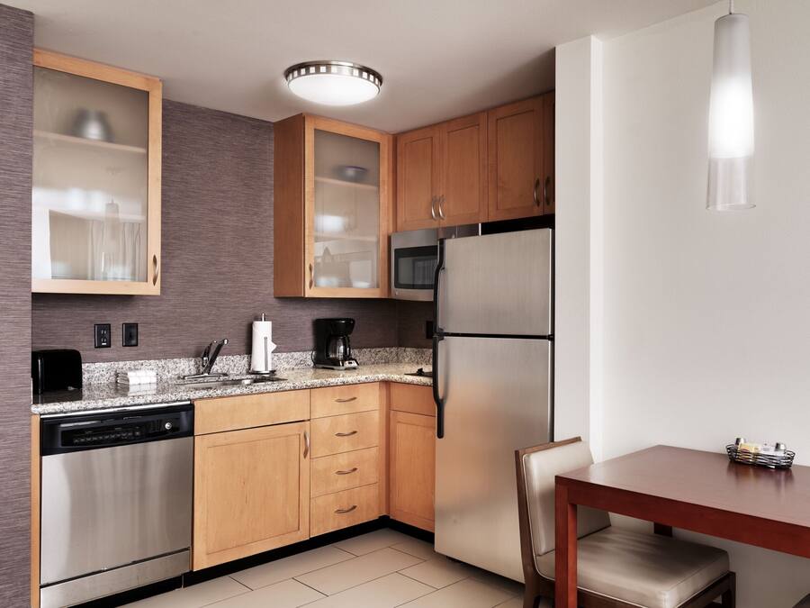 A compact kitchen with wooden cabinets, a built-in microwave, a stainless steel refrigerator, and a dishwasher.