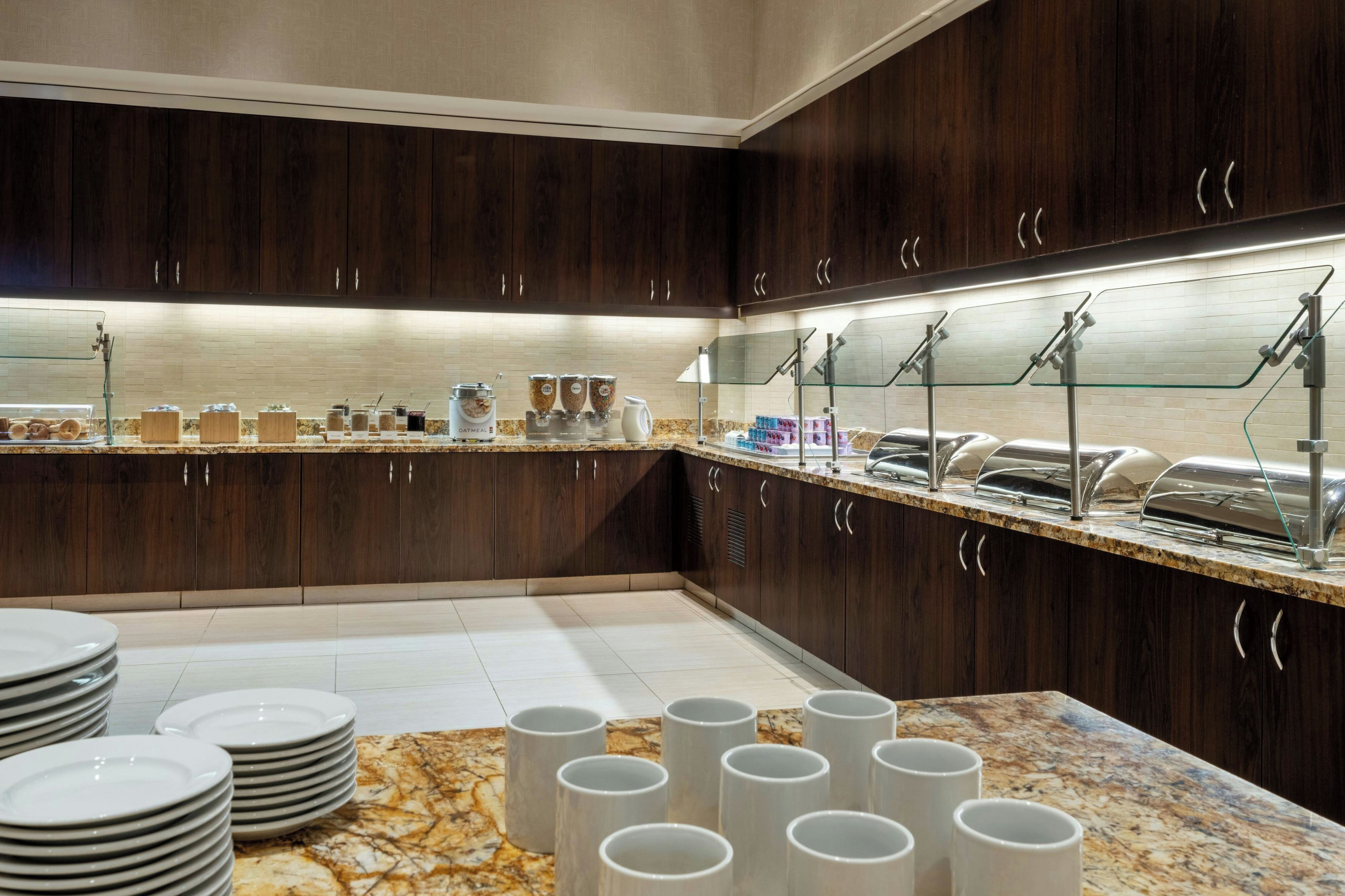 A modern kitchen with dark wood cabinets, a marble countertop, and a buffet area with various food items.