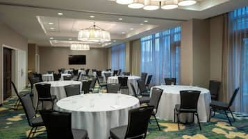 Un salón de conferencias con mesas redondas, sillas y un gran ventanal con cortinas.