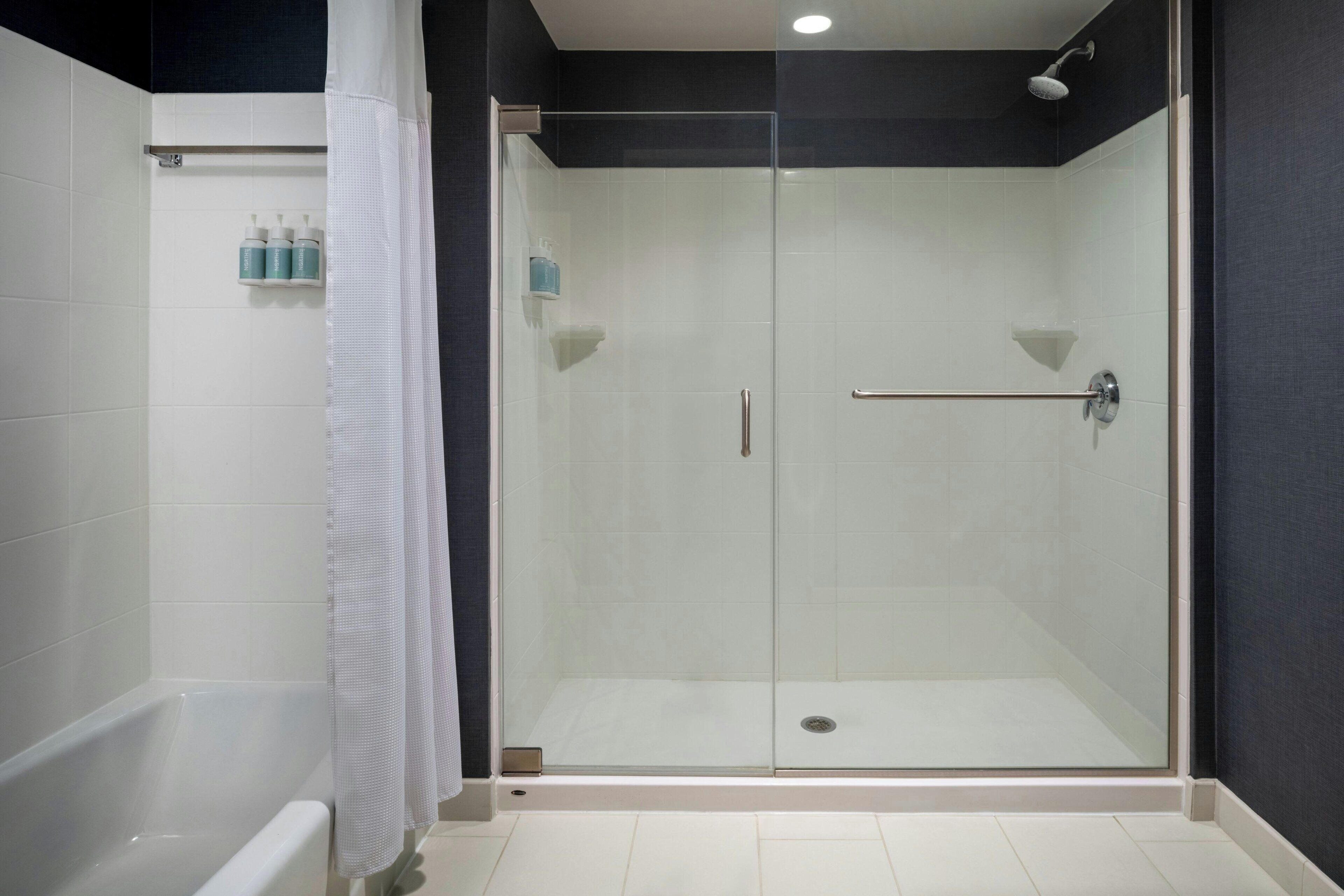 A modern bathroom with a glass-enclosed shower, a white bathtub, and a towel rack with bottles.