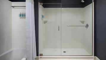A modern bathroom with a glass-enclosed shower, a white bathtub, and a towel rack with bottles.