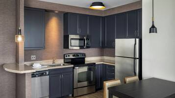 Una cocina moderna con armarios oscuros, electrodomésticos de acero inoxidable, horno empotrado, microondas y refrigerador.
