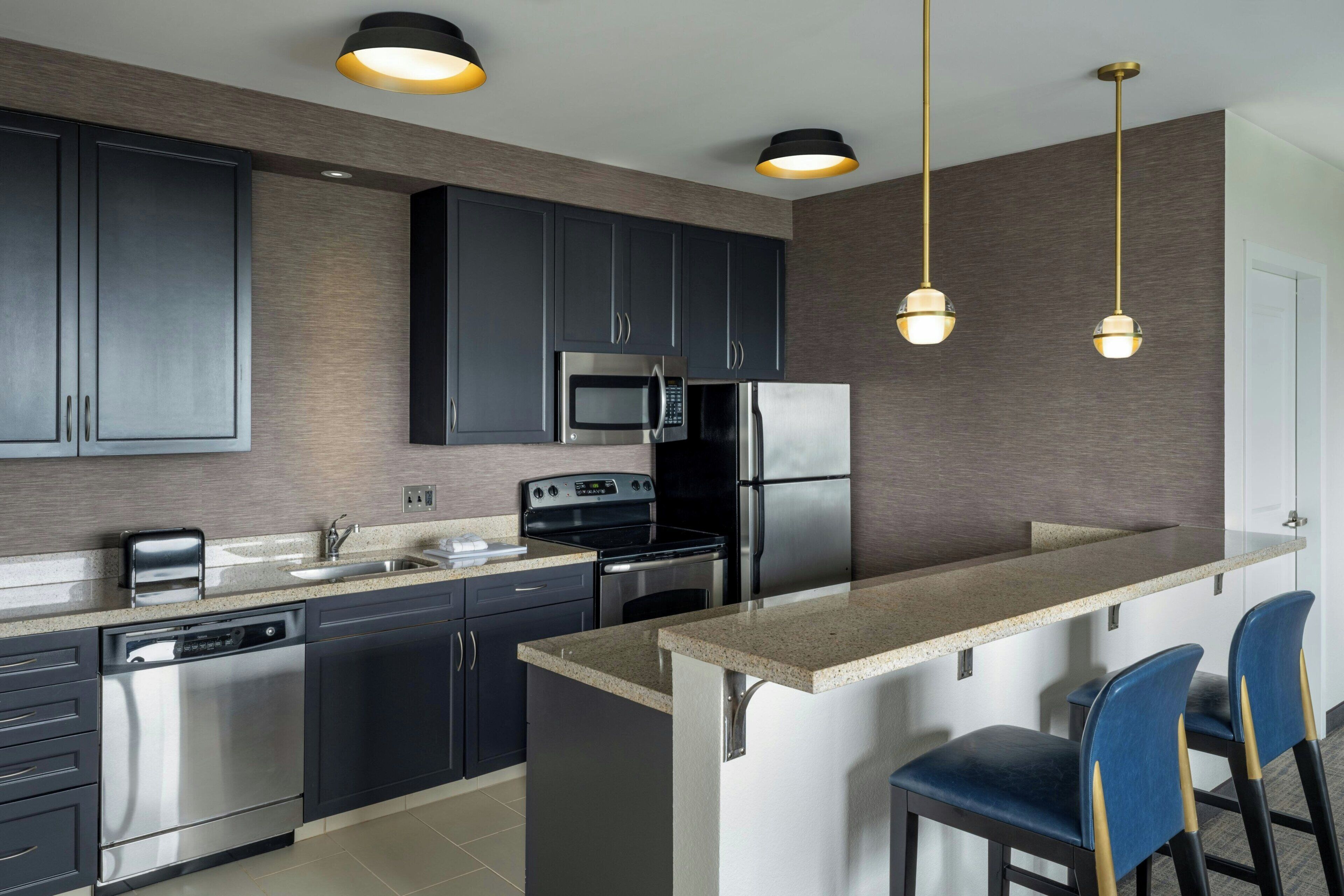 A modern kitchen with dark cabinets, stainless steel appliances, a granite countertop, and pendant lighting.